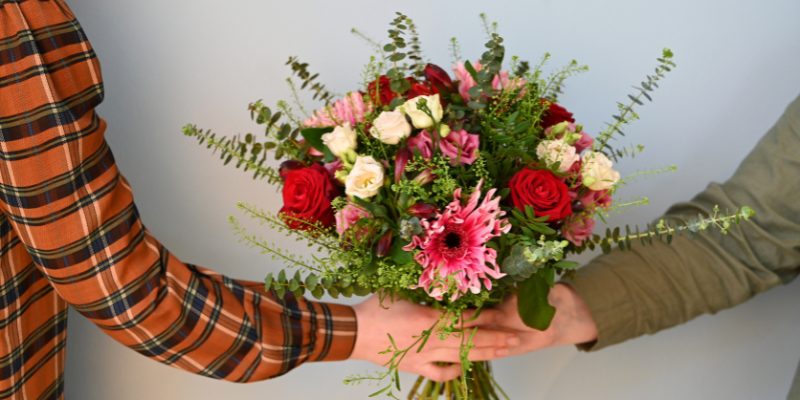 2 der giver hinanden en buket i røde farver, fra hånd til hånd