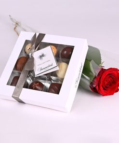 Chokoladeæske og en rød rose pakket i cellofan.