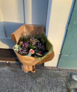 Buket i lilla farver, stående ved en dør og pakket ind til gave.