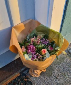 Buket i lilla farver, pakket ind til og stillet ved dør.