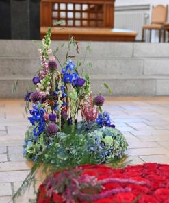 Begravelseskrans i blå og lilla nuancer med et rødt blomsterhjerte liggende foran