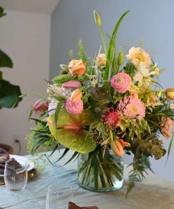 Buket med tulipaner, anthurium, deko chrys, ranunkler, valmuer og andet i sarte farver på bord med grøn dug