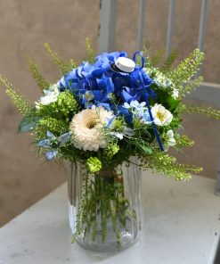 En tæt buket med blå og hvide blomster pyntet med en passende blå studenterhue