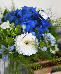 Nærbillede af en blå og hvid buket med en lille blå studenterhue som pynt