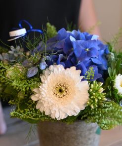 Buket i hvide og blå nuancer med en blå studenterhue og person i baggrunden