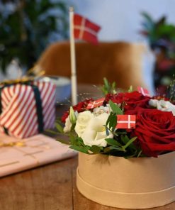 Blomsteræske med røde og hvide blomster, står på bord sammen med gaver og flag