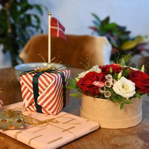 Blomsteræske med røde og hvide blomster, står på bord sammen med gaver og flag