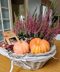 Kurv med lyngplanter, græskar og chokolade står på bord af træ