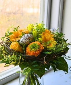 En orange påskebuket med påskeæg i midten og pyntet med små grene