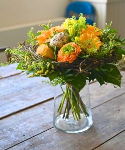 Billede af en orange og gul buket i glasvase på et rustikt bord.