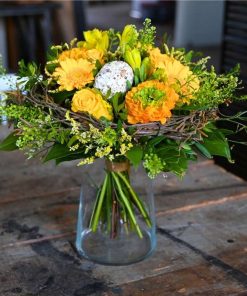 En påskebuket i orange og gule farverp pyntet med påskeæg i midten på et rustikt bord.