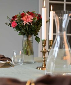 Bord dækket op med levende lyse og en buket i lyserøde og røde farver i baggrunden