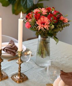 Bord dækket op med levende lys og en buket i røde og lyserøde farver i høj glasvase.