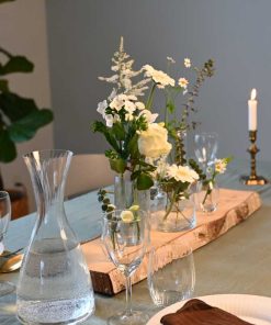 Små vaser med forskellige blomster i hvide farver placeret på en stamme af birketræ, på dækket middagsbord