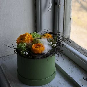 En påskeblomsteræske med orange blomster stående i en vindueskarm