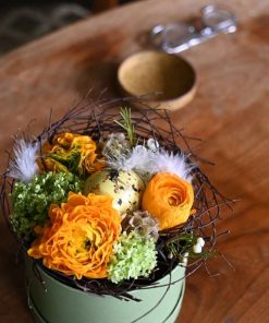 Blomsteræske i gule nuancer med små hvide fjer og et plettet påskeæg i midten