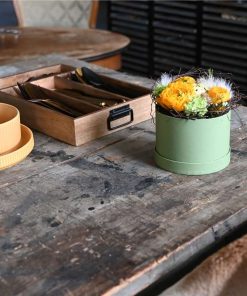 Påske blomsteræske med orange blomster og fjerd på et rustiktbord og bestik i baggrunden