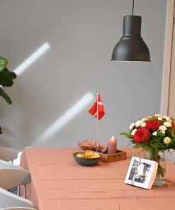 Buket i røde og hvide farver står på et bord med rosa dug, hvor der er dækket op til gæster med flag, lys, øl, chips mv.