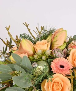 Julebuket i ferskenfarver blomster, som amaryllis, roser og gerbera med sartfarvede grønne blade og pynt