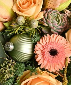 Julebuket i ferskenfarver blomster, som amaryllis, roser og gerbera med sartfarvede grønne blade og pynt