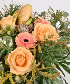 Julebuket i ferskenfarver blomster, som amaryllis, roser og gerbera med sartfarvede grønne blade og pynt