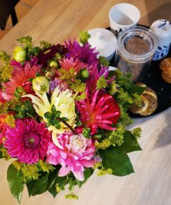 Buket i friske lyserøde og pinke toner set oppefra med en morgenmadstallerken ved siden af