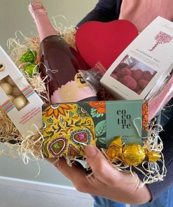 Gavekasse med rosevin og forskellige slags slik og chokolade holdes af person