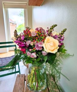 Buket i lys orange med bordeaux farver foran grøn væg