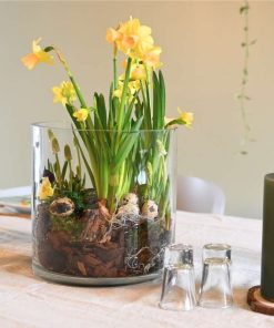 Påskedekoration i gule farver stående på et bord med snapsglas og stearinlys