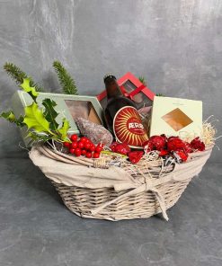 En flettet kurv med øl, slik og chokolade pyntet med julegrene og kogle