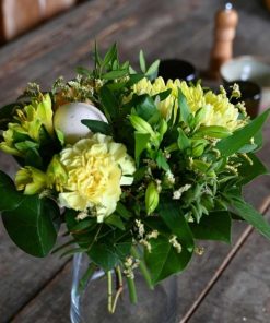 Buket i sarte gule nuancer stående på et bord med kværn i baggrunden