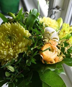 Nærbillede af gul chrysanthemum, sart orange ranunkel og hvidt påskeæg.