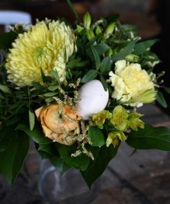 Buket med gule blomster og et hvidt påskeæg som pynt i midten af buketten