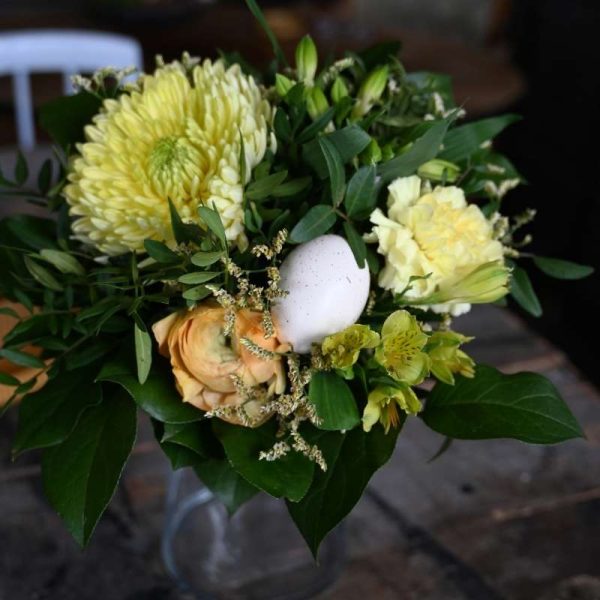 Buket med gule blomster og et hvidt påskeæg som pynt i midten af buketten