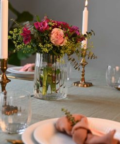 En buket i lilla og lyserøde farver på et bord med levende lys og lyserød opdækning