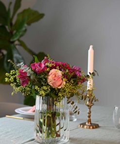 Buket i lilla og lyserøde farver i glasvase på et bord med lys i baggrunden