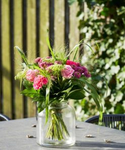 Buket med lyserøde og lilla blomster på et havebord udenfor i solskin