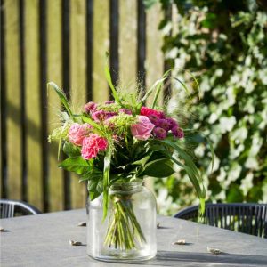 Buket med lyserøde og lilla blomster på et havebord udenfor i solskin