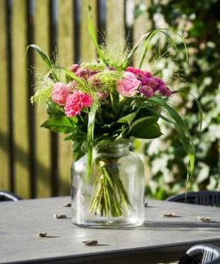 Buket med lyserøde og lilla blomster på et havebord udenfor i solskin