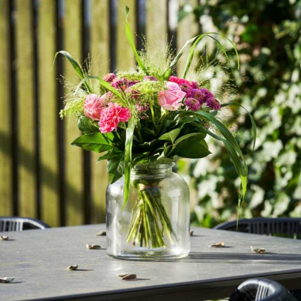 Buket med lyserøde og lilla blomster på et havebord udenfor i solskin