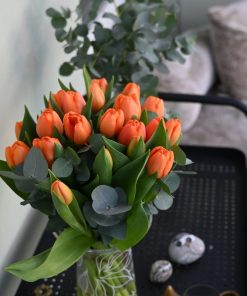 Buket orange tulipaner i en gennemsigtig glasvase, der står på et sort rullebord i hjemlige omgivelser.