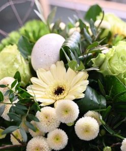 Nærbillede af et hvidt påskeæg i midten af en buket i sarte gule farver