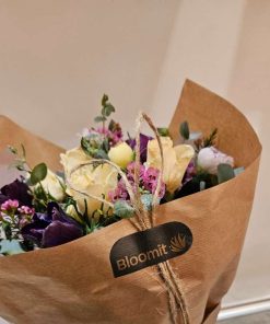 Buket med roser, ranunkler og franske anemoner pakket ind