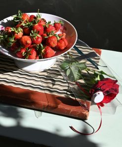 Billede af en rød studenterhue og en rød rose set oppefra med en skål jordbær ved siden af