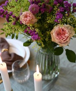 En lilla og lyserød buket på et bord med levende lys og opdækning