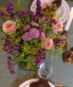 En lilla og lyserød buket på et bord med levende lys og opdækning