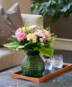 En buket i lyse farver på et fad med to glas og sofa i baggrunden