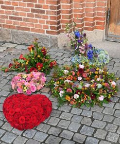 En begravelseskrans med opsats, rødt blomsterhjerte, begravelseskrans, åbent blomsterhjerte og begravelsesdekoration udenfor kirke
