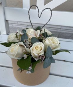 Hvid blomsteræske med hjerte af metaltråd som pynt på en bænk udenfor