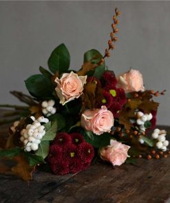 Buket med ferskenfarvede roser, chrysanthemum , snebær og efterårsgrene liggende på brunt rustikt bord